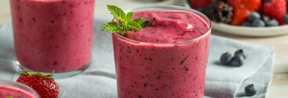Berry protein smoothie in a glass garnished with mint on a napkin with fresh strawberries and blueberries in the background