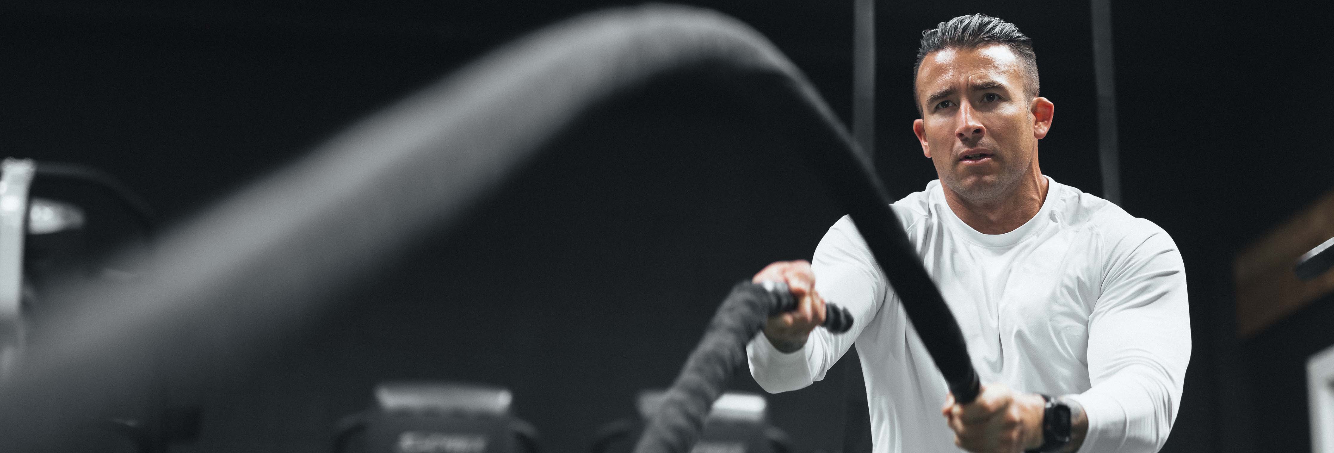 Man doing a battle rope workout in a gym, intense expression and dark background