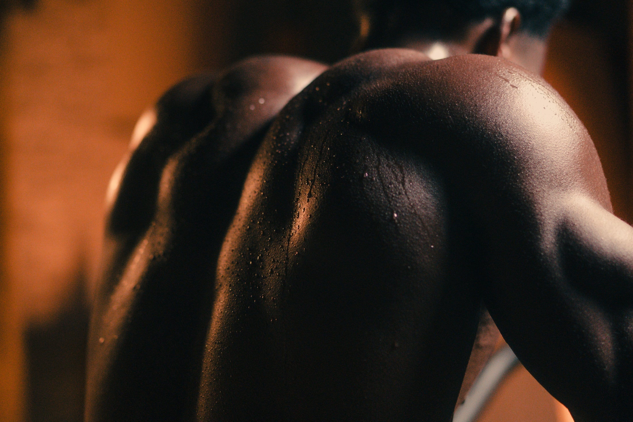 Close-up of a sweaty, muscular person's back and shoulders lit by warm studio light