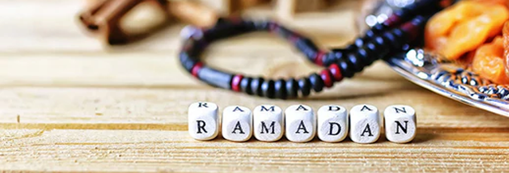 Close-up of letter blocks spelling Ramadan beside prayer beads and a plate of dates on a wooden table