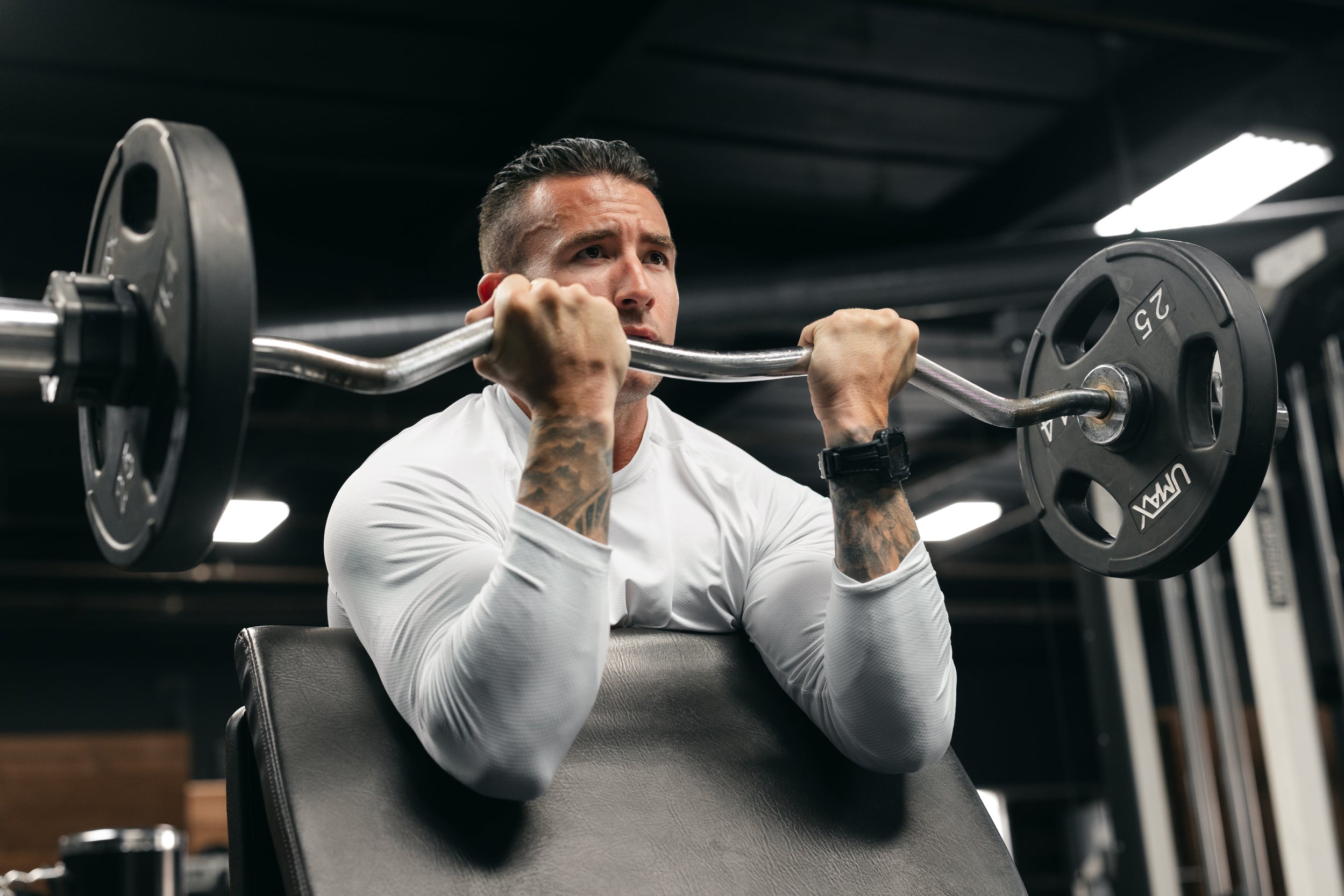 Man performing preacher curls with an EZ curl bar on a gym bench, focused expression