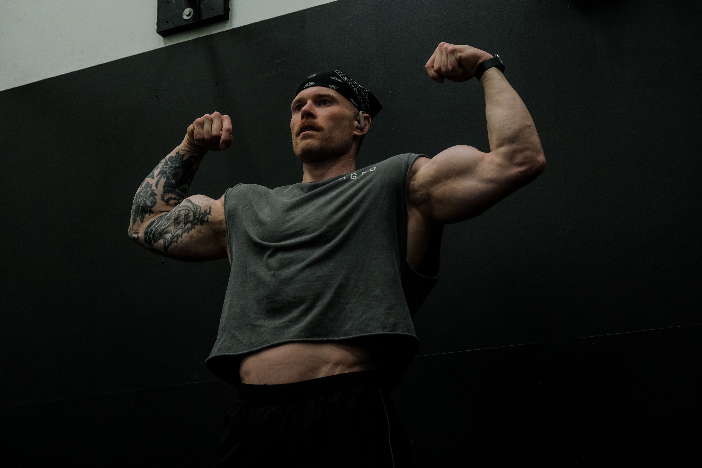 Man flexing both arms to show defined triceps in a dimly lit gym against a black wall