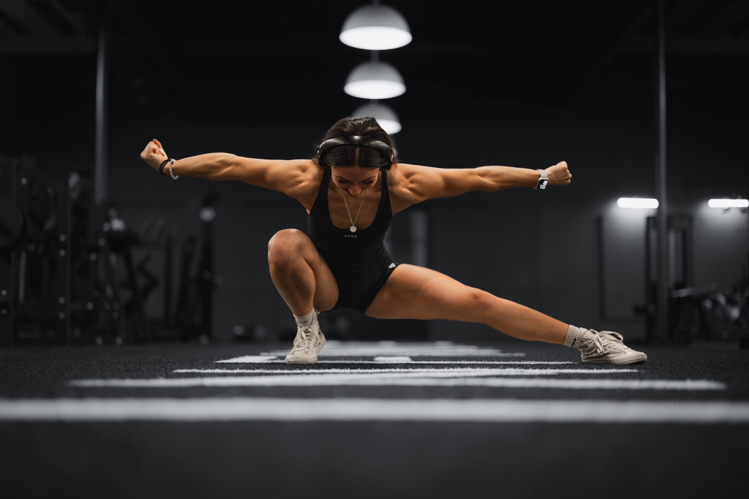 Female athlete performing a deep lateral lunge on gym turf, arms extended for balance, low angle dimly lit training facility