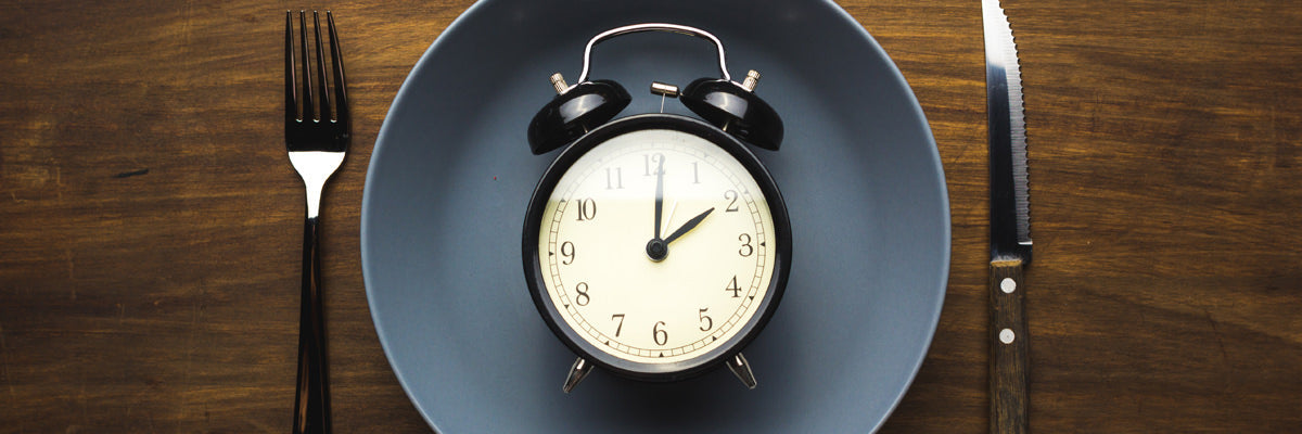 Alarm clock on a plate between a fork and knife symbolizing fasting and meal timing