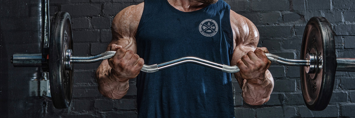 Muscular man performing barbell curls in a gym against a dark brick wall