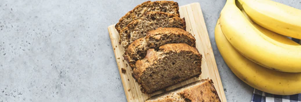 Sliced banana bread on a wooden cutting board with ripe bananas on a gray countertop