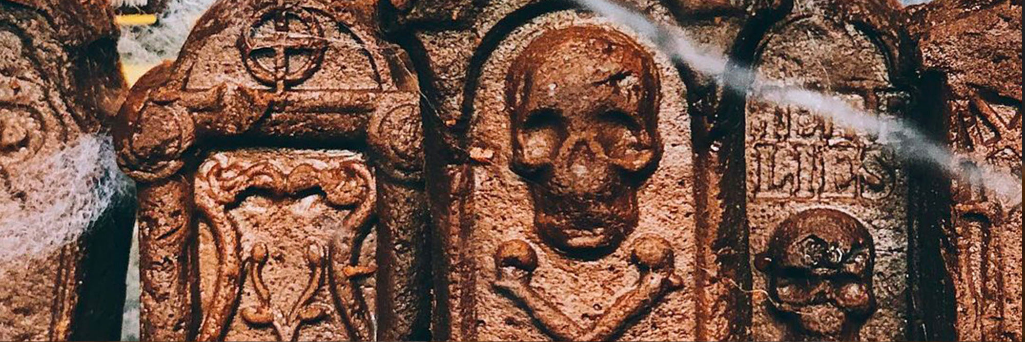 Close-up of tombstone-shaped chocolate protein brownies showing carved skull-and-crossbones decorations and faux cobwebs