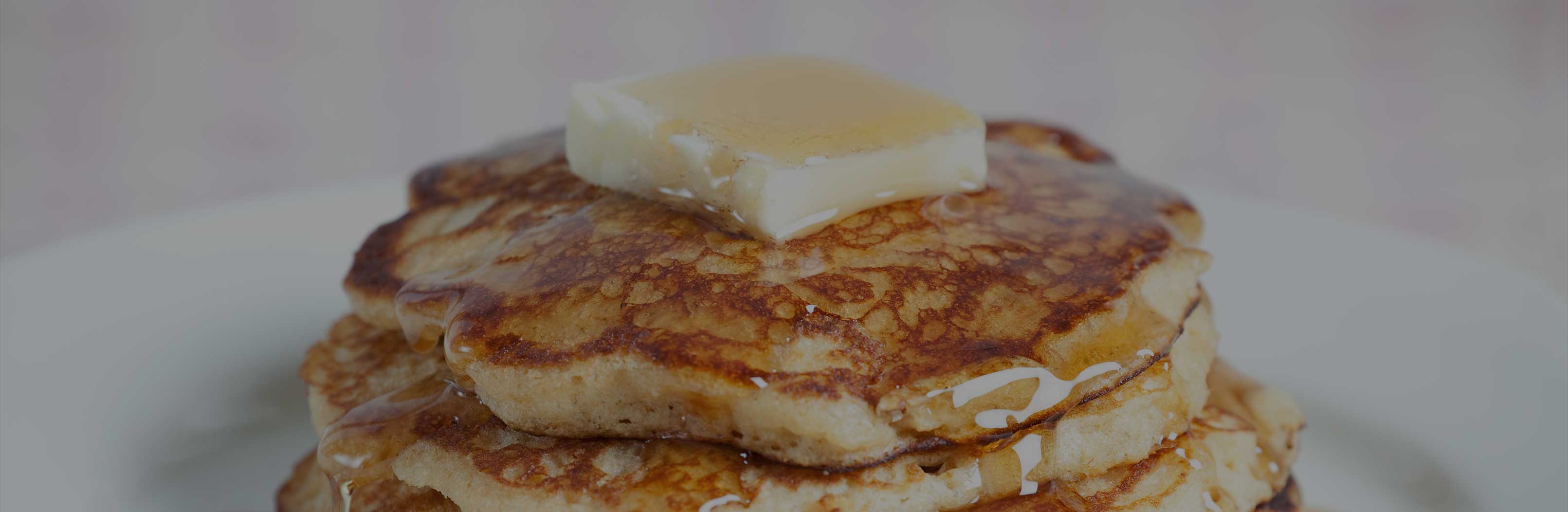 Close-up of stacked peanut butter cookie protein pancakes topped with melting butter and drizzled maple syrup on a white plate