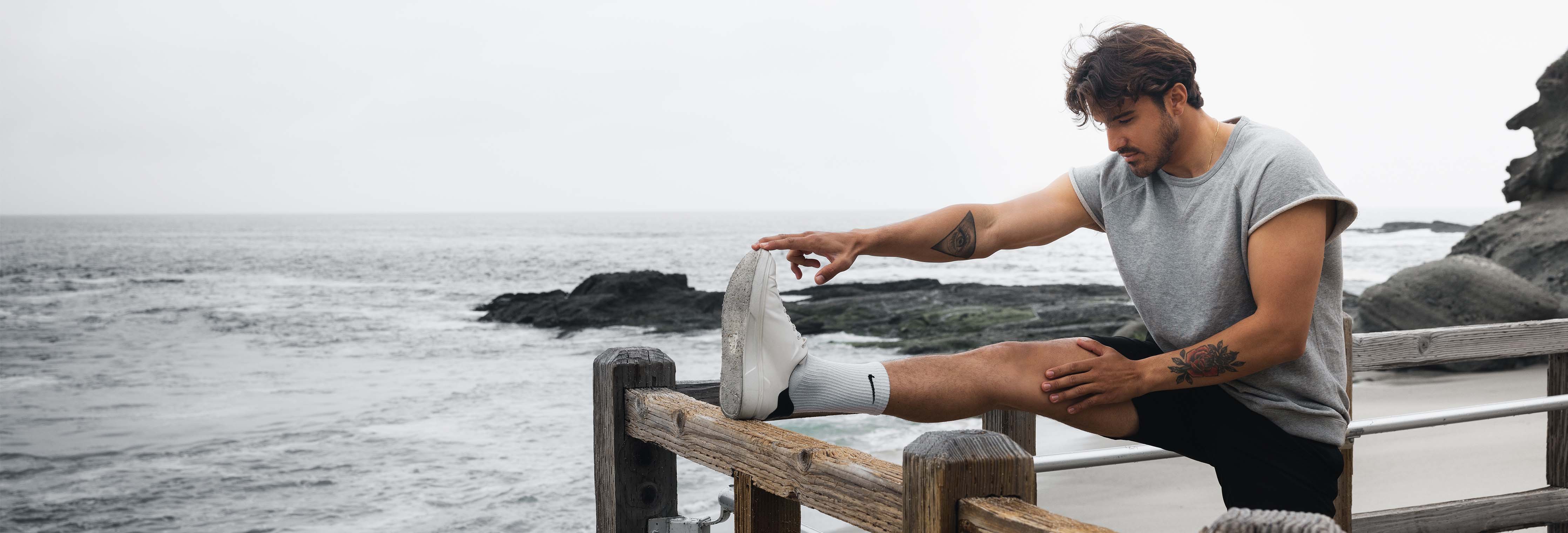 Man stretching his leg on a wooden railing overlooking a rocky ocean shore