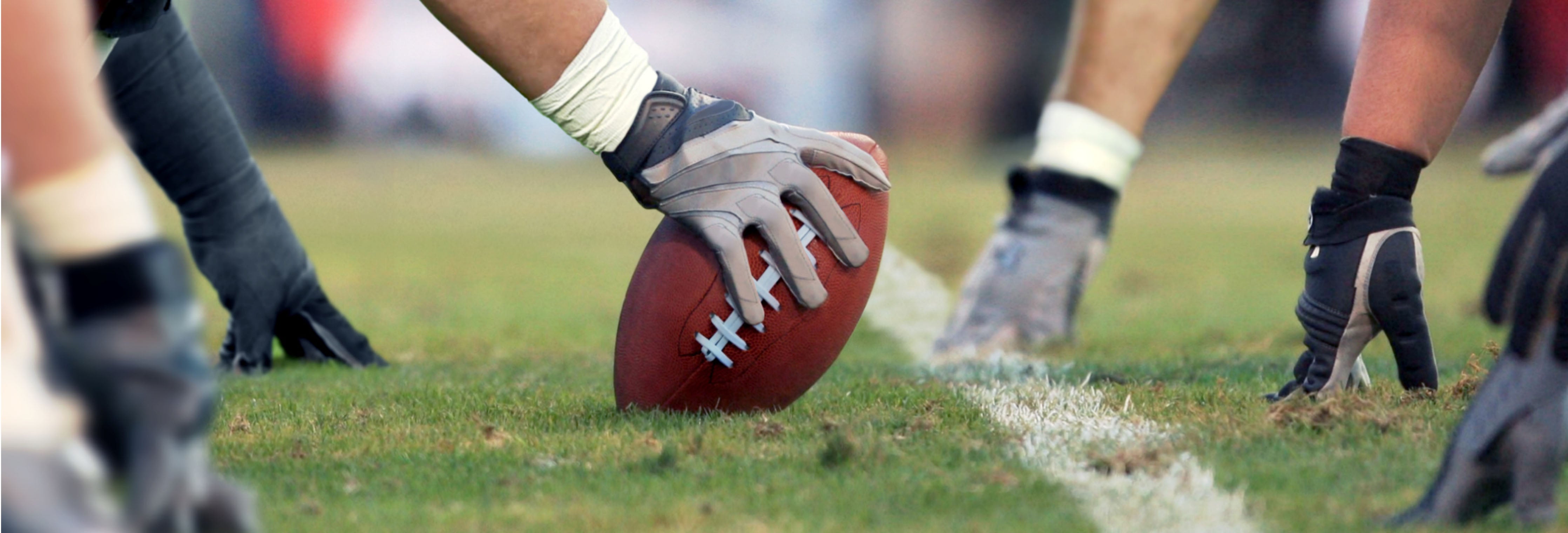 Center placing a football on the line of scrimmage with players' hands and cleats on a grass field