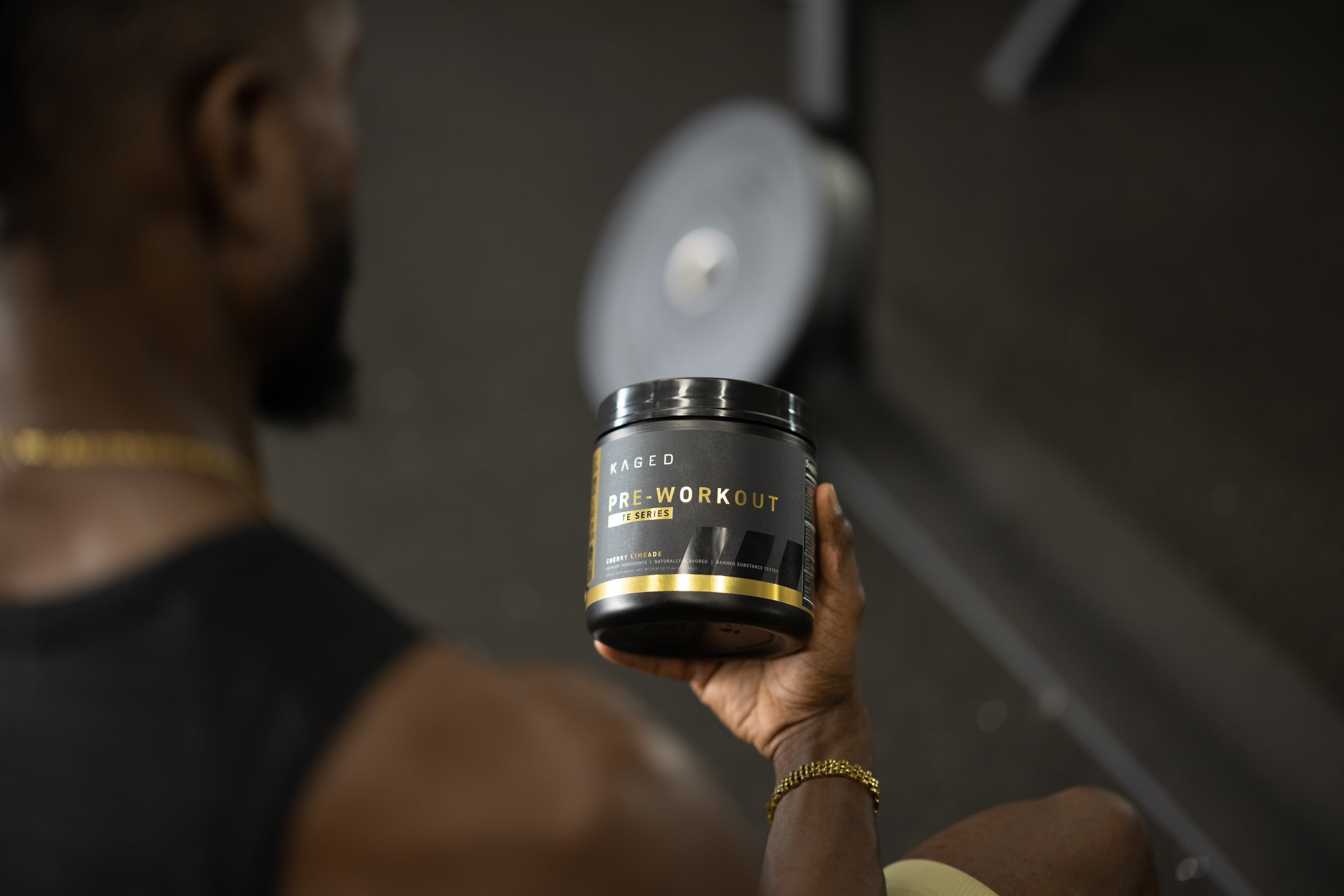 Man holding KAGED Pre-Workout jar in a gym with jar label reading PRE-WORKOUT and a weight plate in the background
