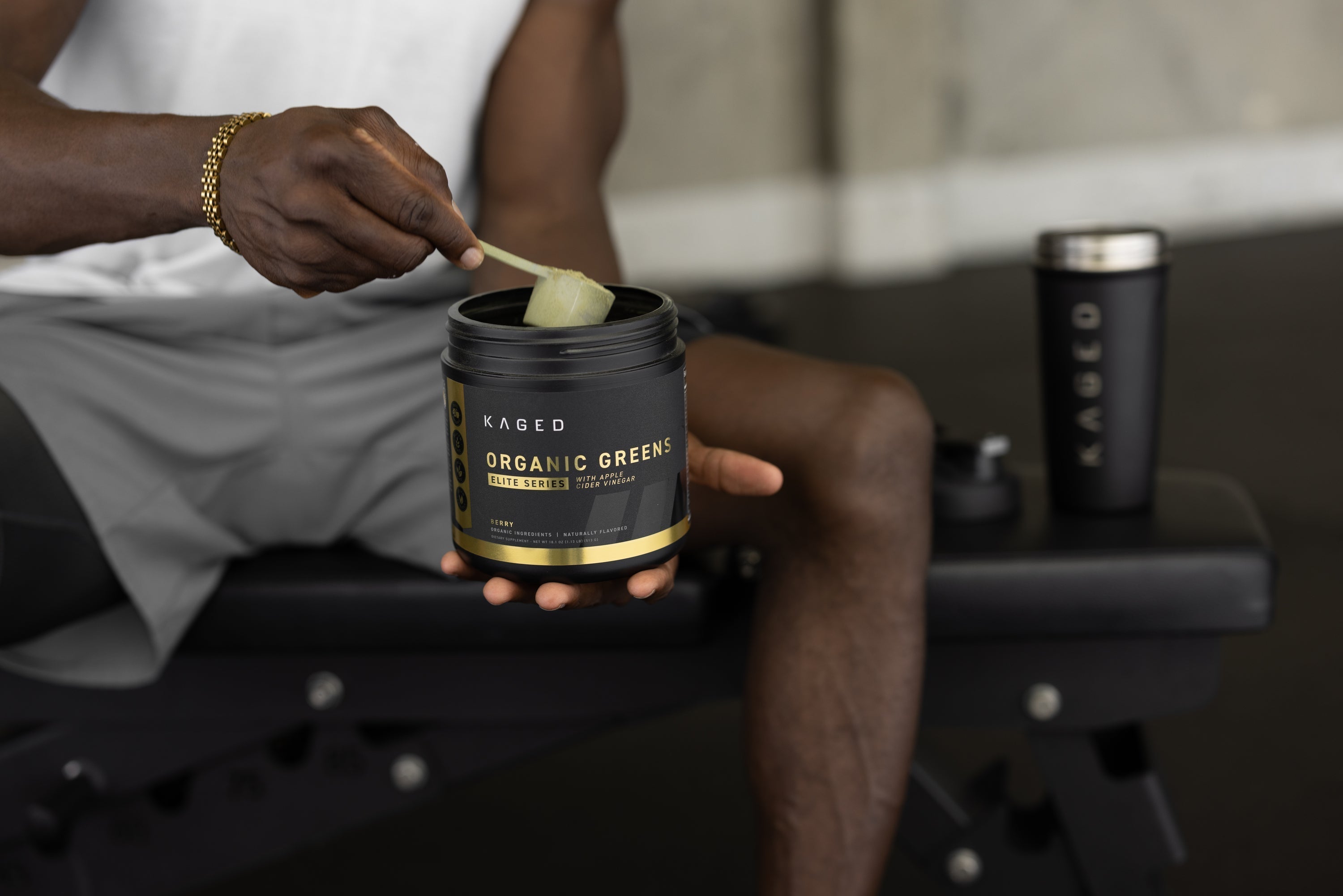 Close-up of KAGED Organic Greens tub with scoop of green powder, held on bench with KAGED shaker cup in background