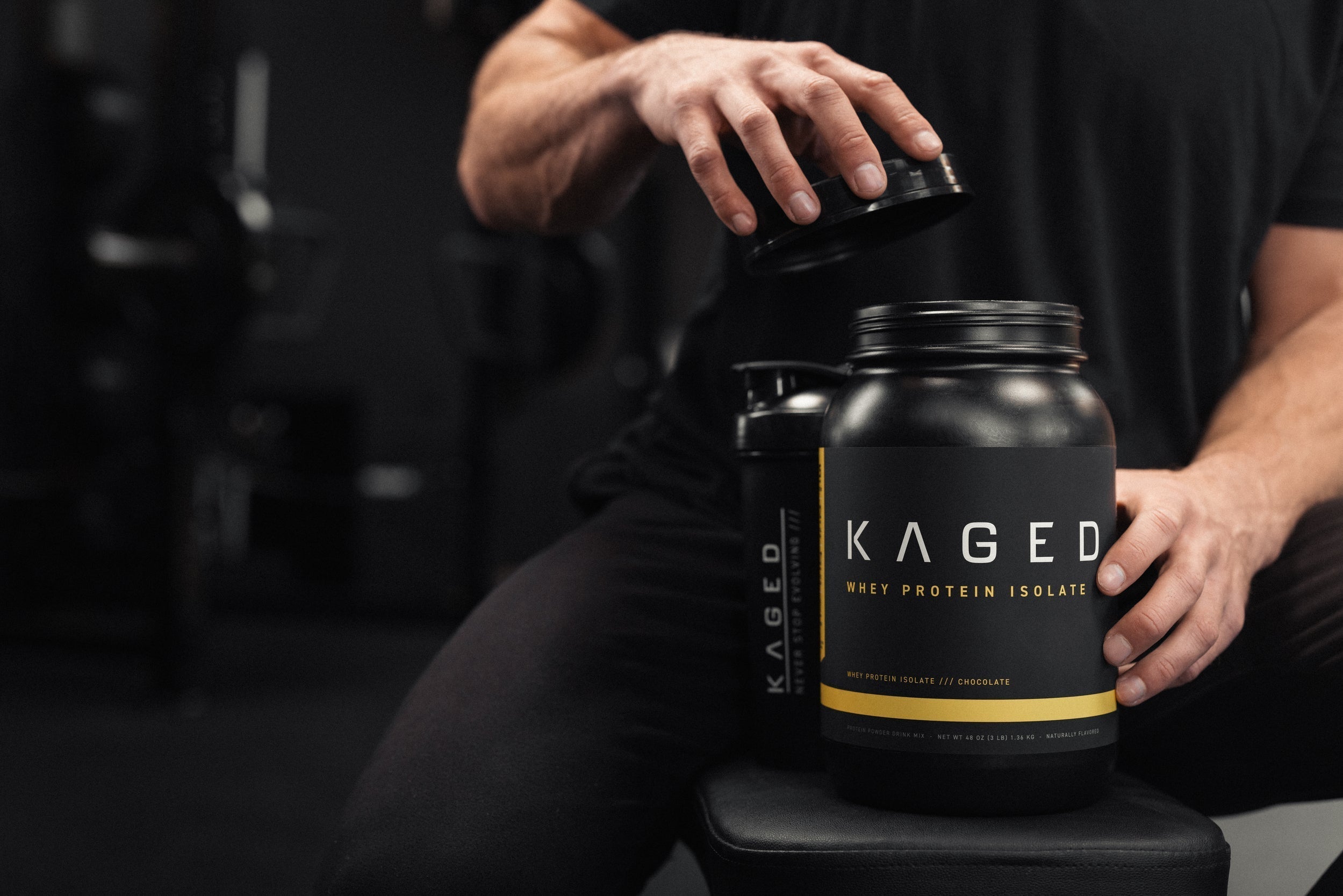 Person opening a KAGED Whey Protein Isolate tub in a dark gym setting