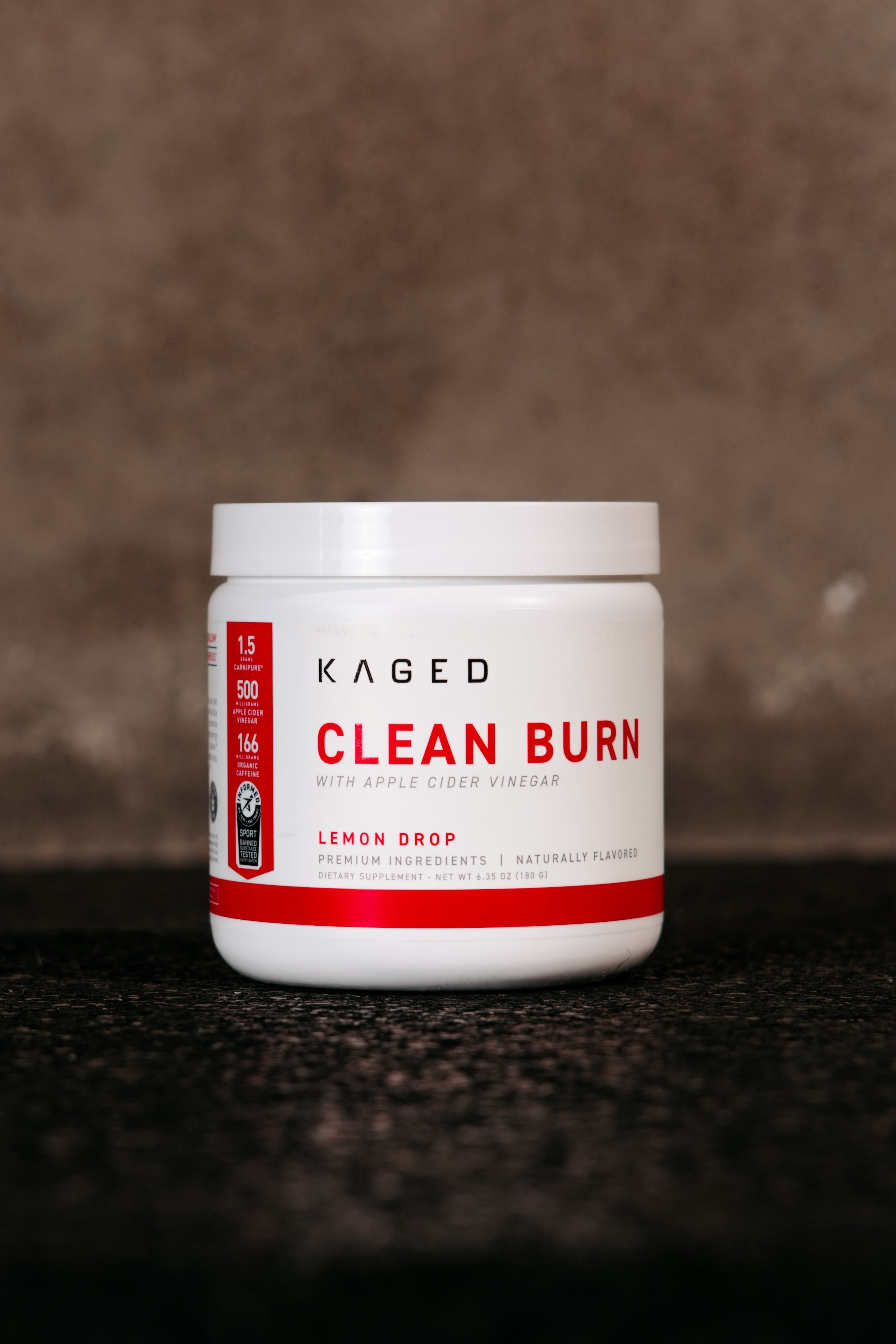 Front view of KAGED Clean Burn supplement jar showing red CLEAN BURN label and apple cider vinegar callout on dark textured background