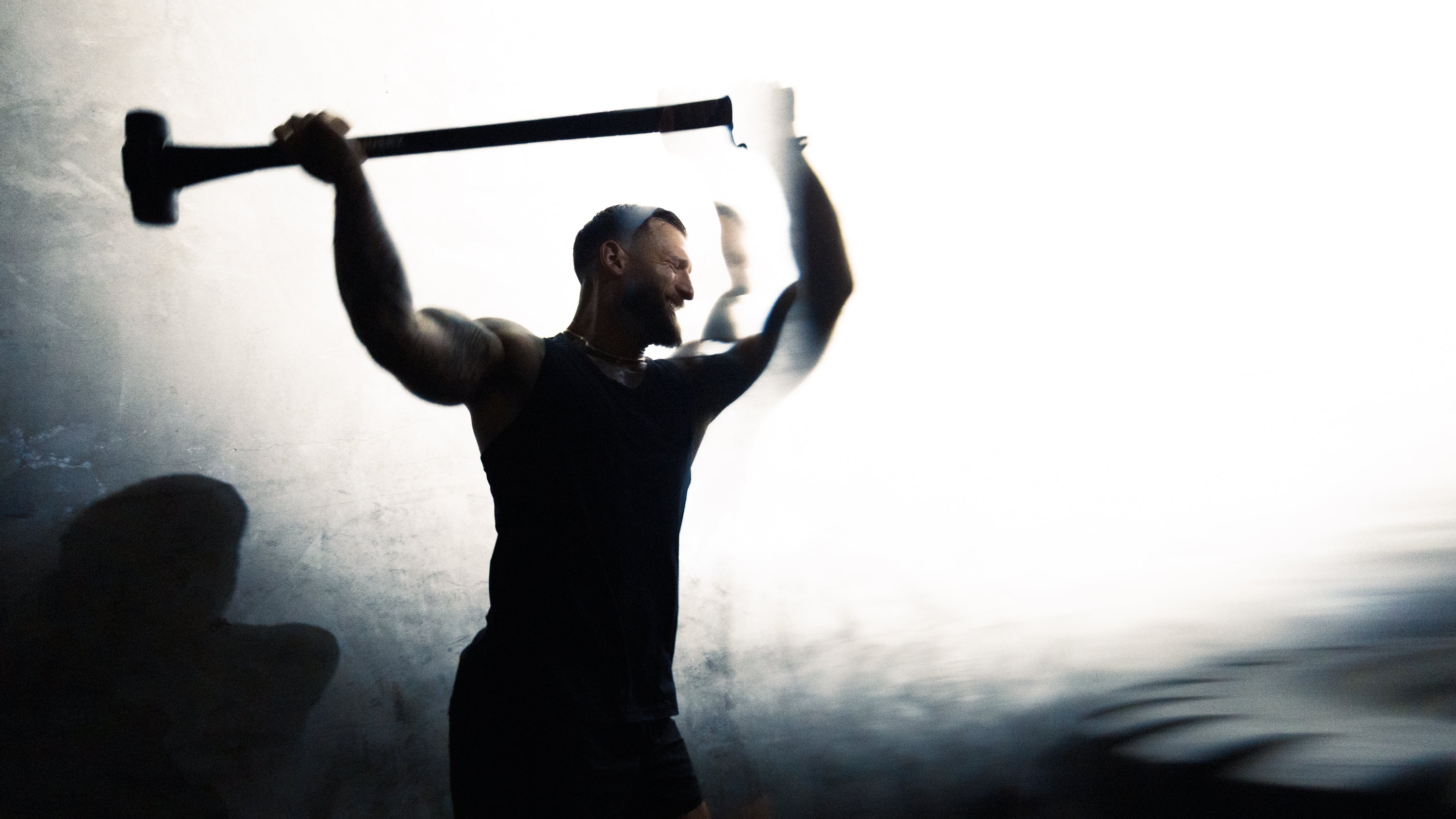 Muscular man swinging a sledgehammer during intense training in a dim gym, motion blur conveying power and conditioning