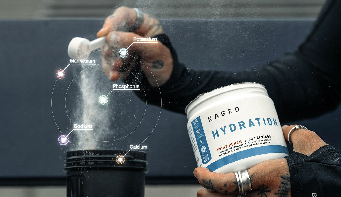 Person scooping KAGED Hydration powder into a shaker with electrolytes labeled Na, K, Mg, Ca, P