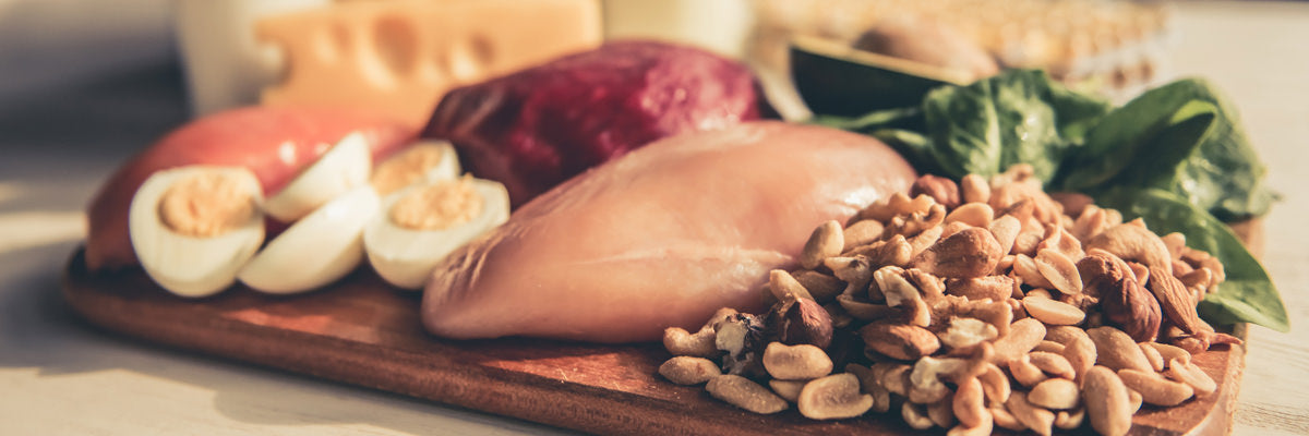 Raw chicken breast, boiled eggs, mixed nuts, beets, and leafy greens on a cutting board representing protein and healthy fats