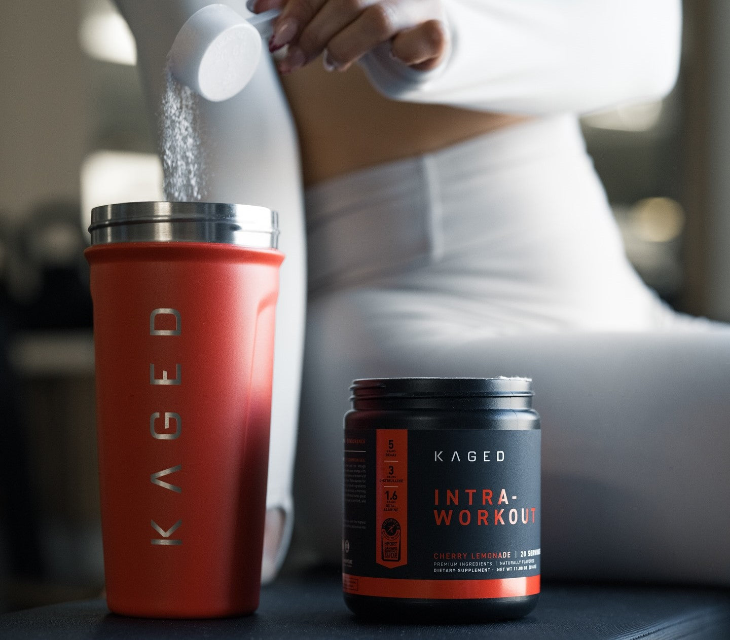 A woman in white sportswear making a Kaged intra-workout drink in a gym setting.
