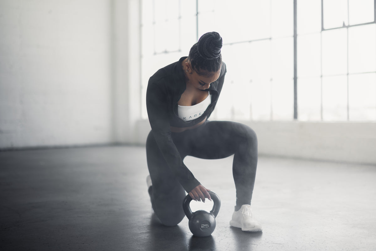 Athlete kneeling to grip a 25 lb kettlebell in a sunlit warehouse-style gym