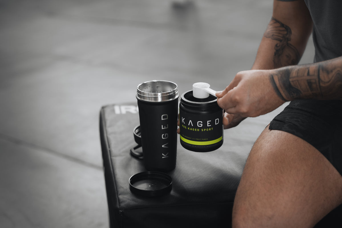 Athlete scooping KAGED pre-workout powder into a black KAGED shaker while seated on a gym box