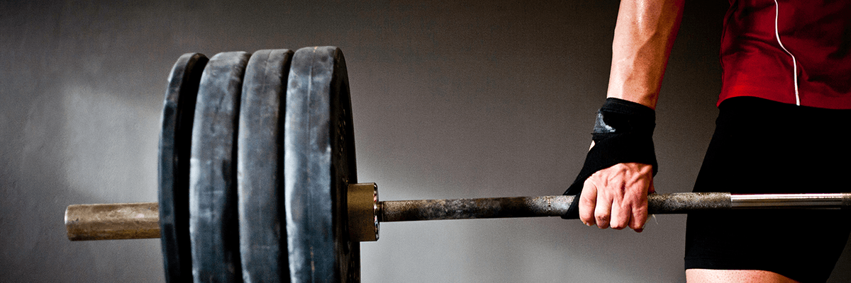 Athlete gripping a heavily loaded barbell, preparing to perform a deadlift in a gym