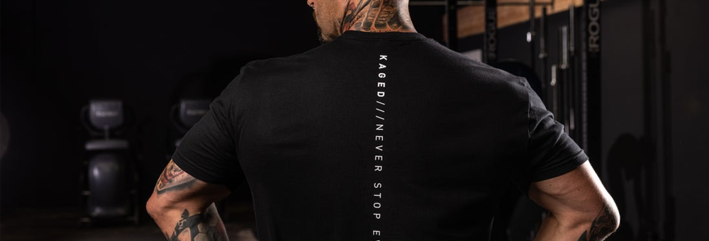 Man showing muscular back in gym wearing black KAGED shirt with vertical KAGED NEVER STOP text