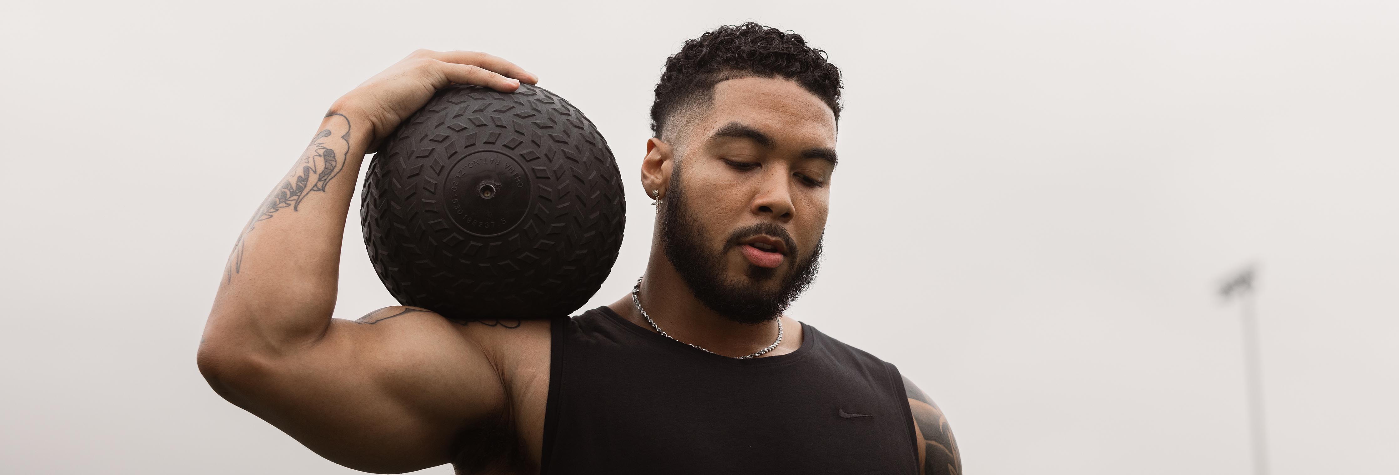 Athletic man holding a textured medicine ball on his shoulder during an outdoor workout