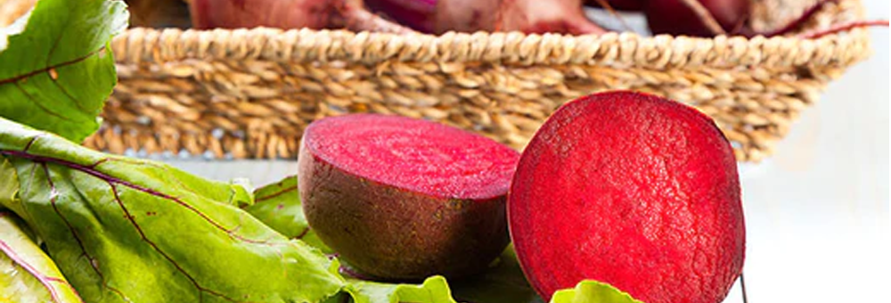 Close-up of halved beetroot and beet greens on a white surface with a wicker basket in the background