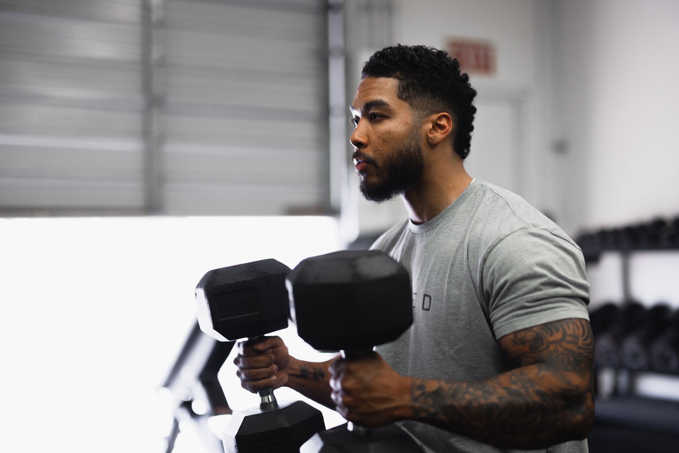 Man doing seated dumbbell chest press in a gym, focused expression with rack of weights in background