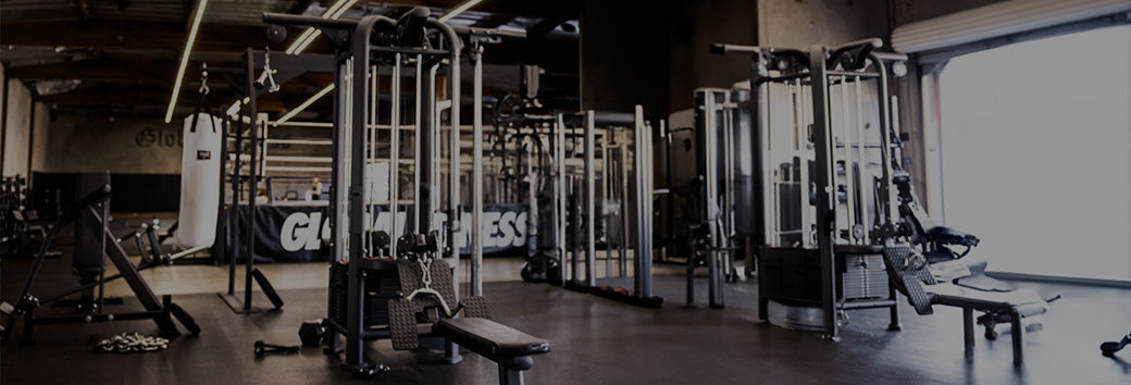 Empty gym showing cable machines, benches, and free weights in an industrial-style training space