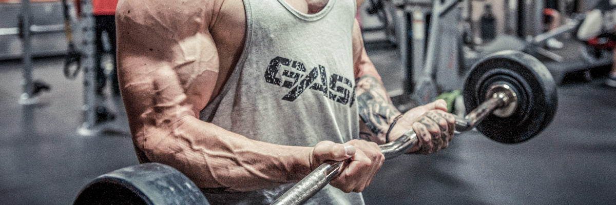 Close-up of a muscular man performing an EZ-bar curl in a gym, emphasis on bulging biceps and veined forearms
