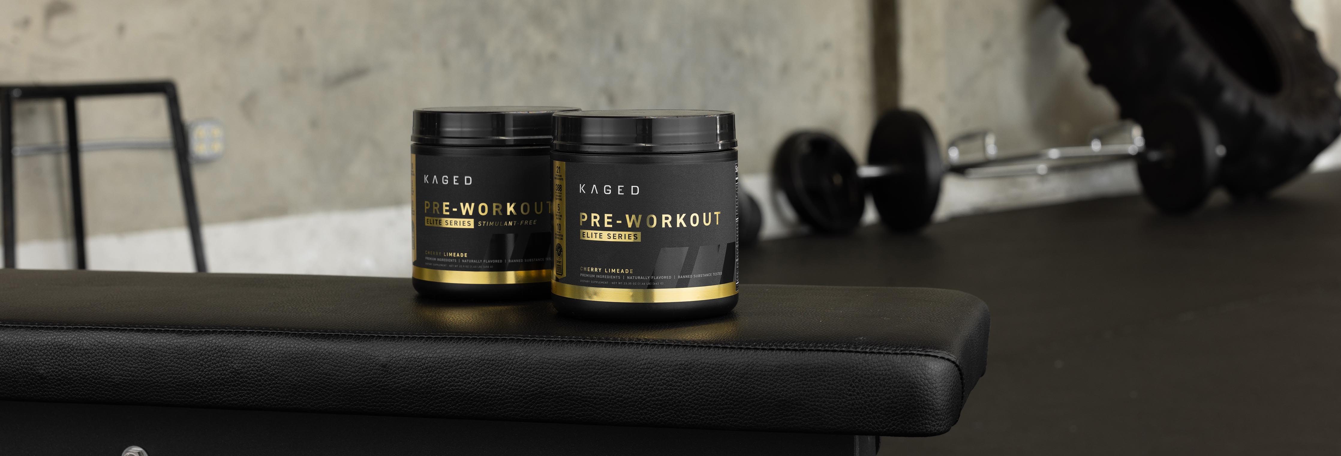 Three-quarter view of two Kaged Pre-Workout tubs with black-and-gold labels on a gym bench and dumbbells in the background