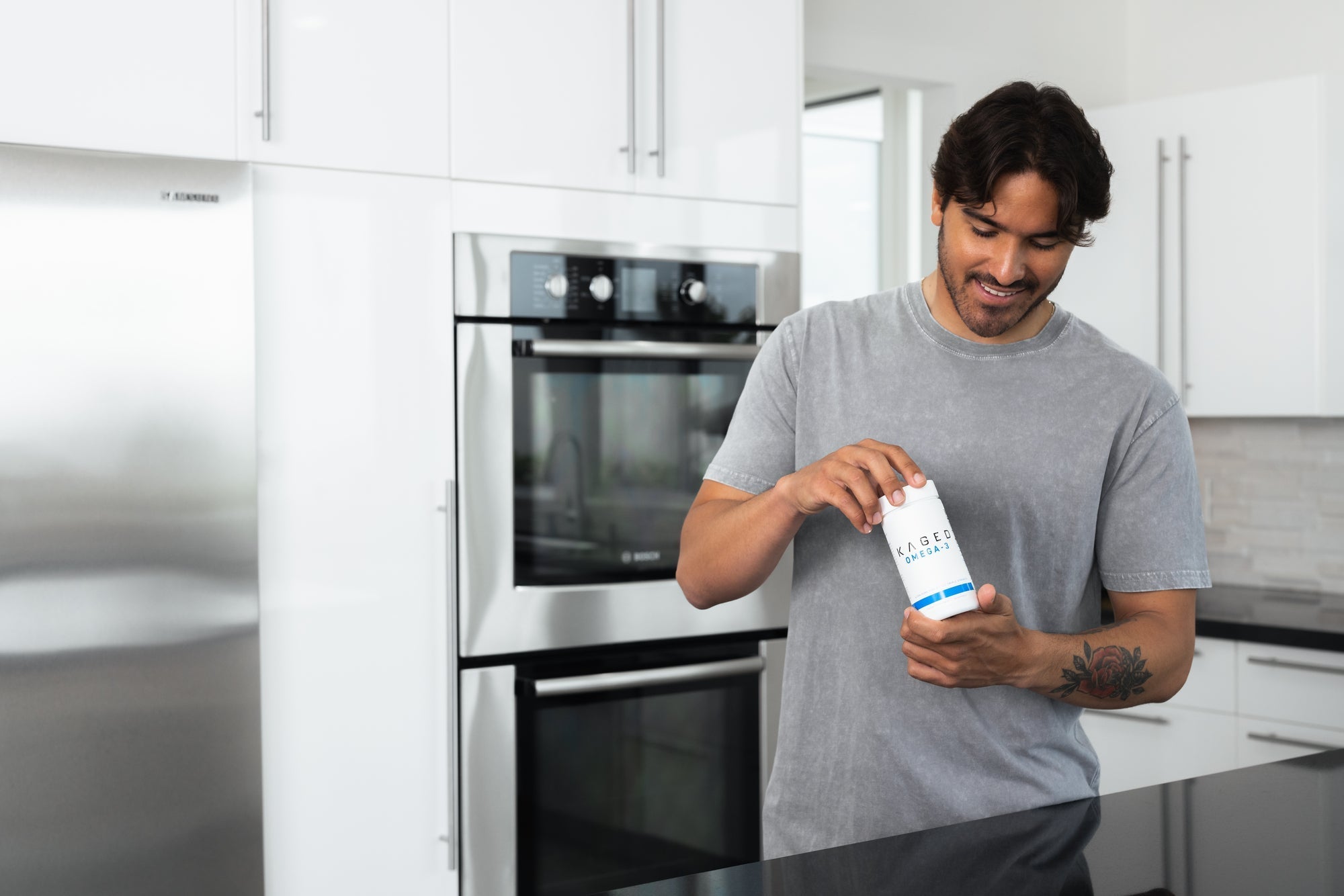 Man opening a KAGED Omega-3 supplement bottle in a bright modern kitchen