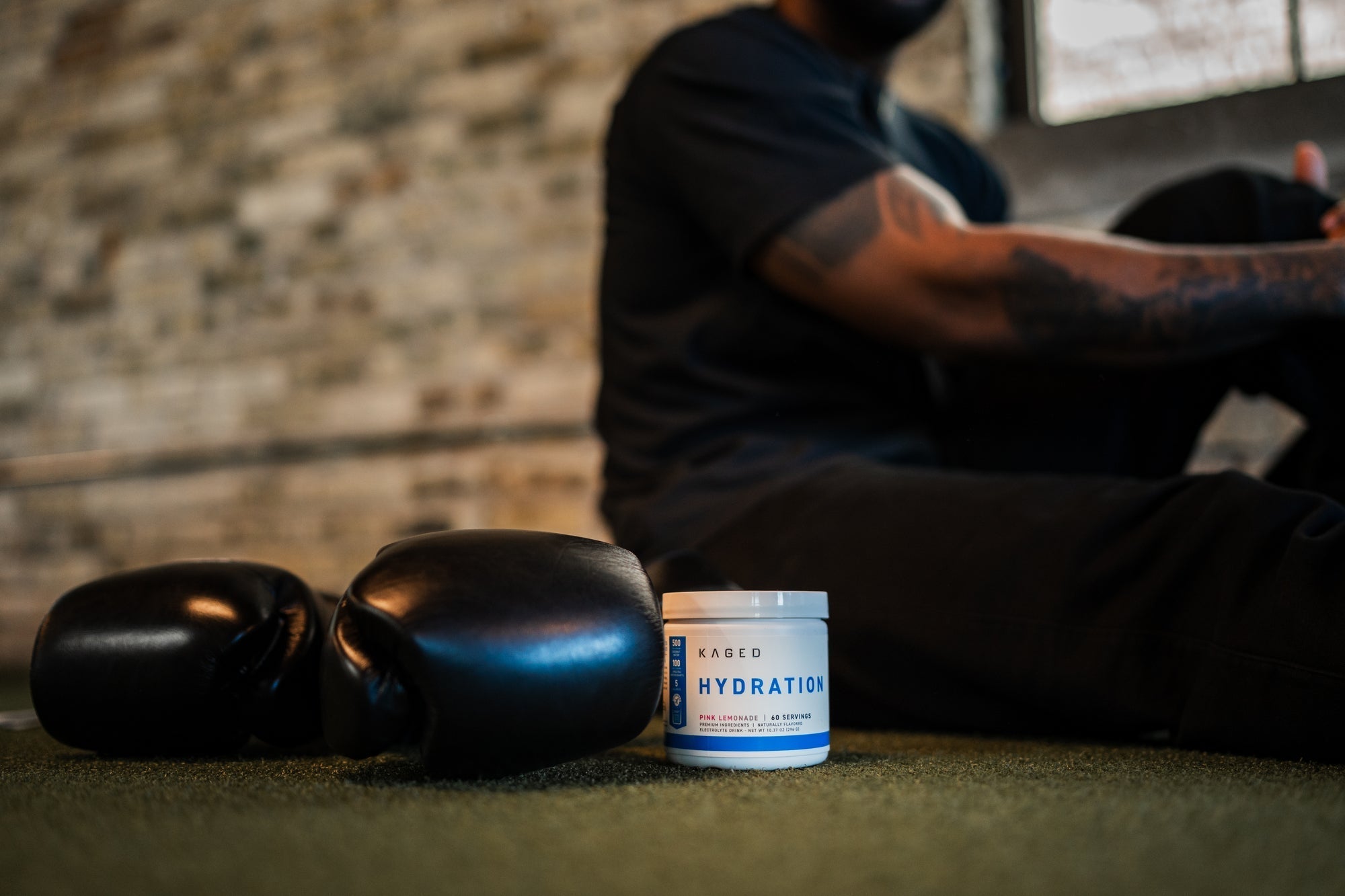 KAGED Hydration tub beside boxing gloves with a seated athlete resting on turf in a gym