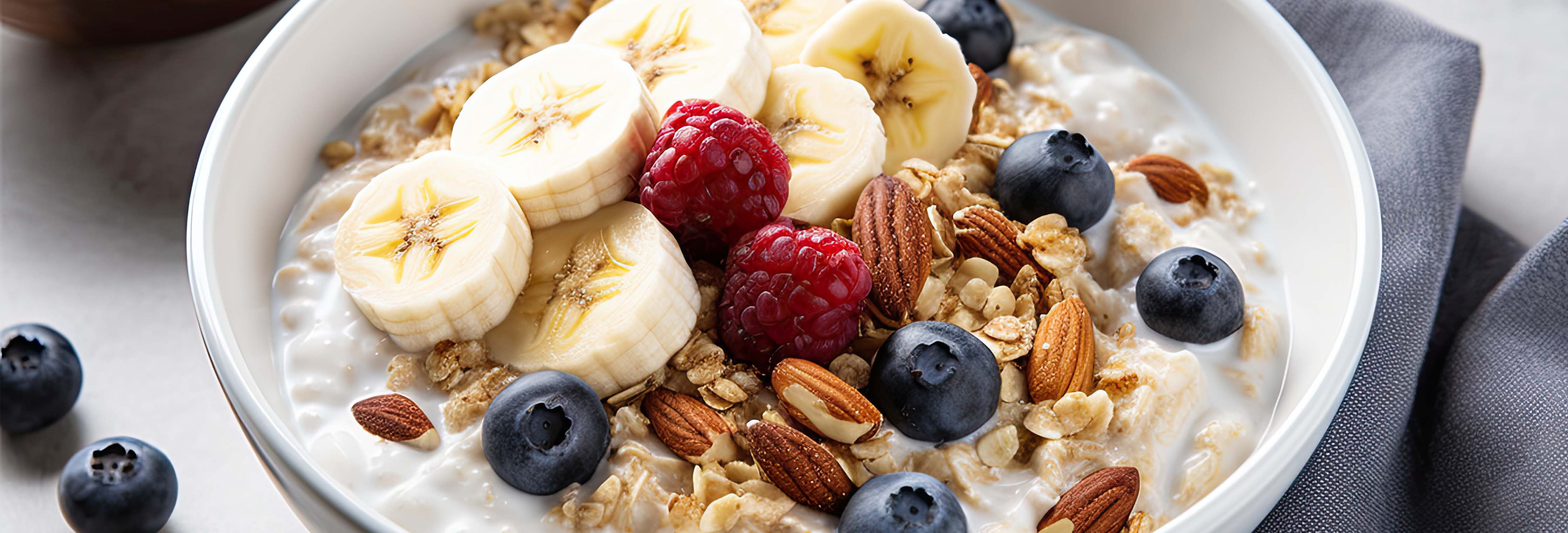 Oatmeal served in a white bowl topped with banana slices, raspberries, blueberries, granola, and almonds on a gray napkin