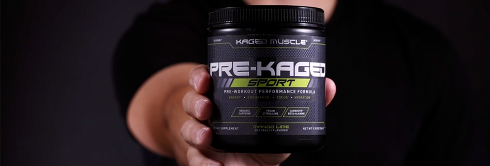 Front view of Pre-Kaged Sport pre-workout tub held in hand, showing product label and mango lime flavor on dark background