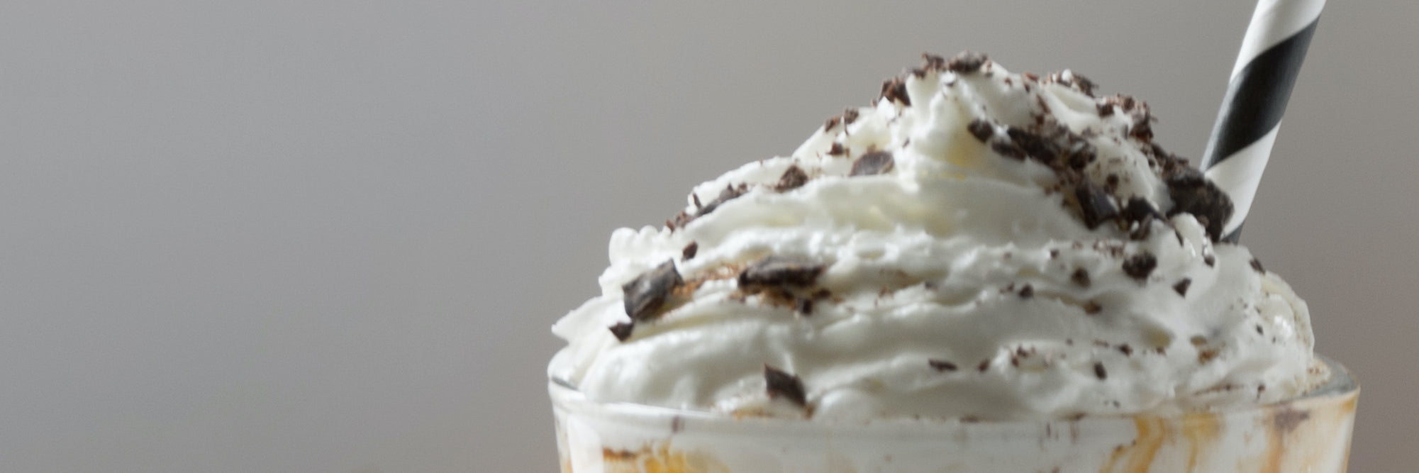 Close-up of pumpkin protein milkshake with whipped cream, chocolate shavings, and a striped straw on a neutral background