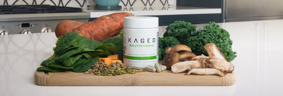 Front view of KAGED Multivitamin jar with capsules and fresh produce on a cutting board in a kitchen