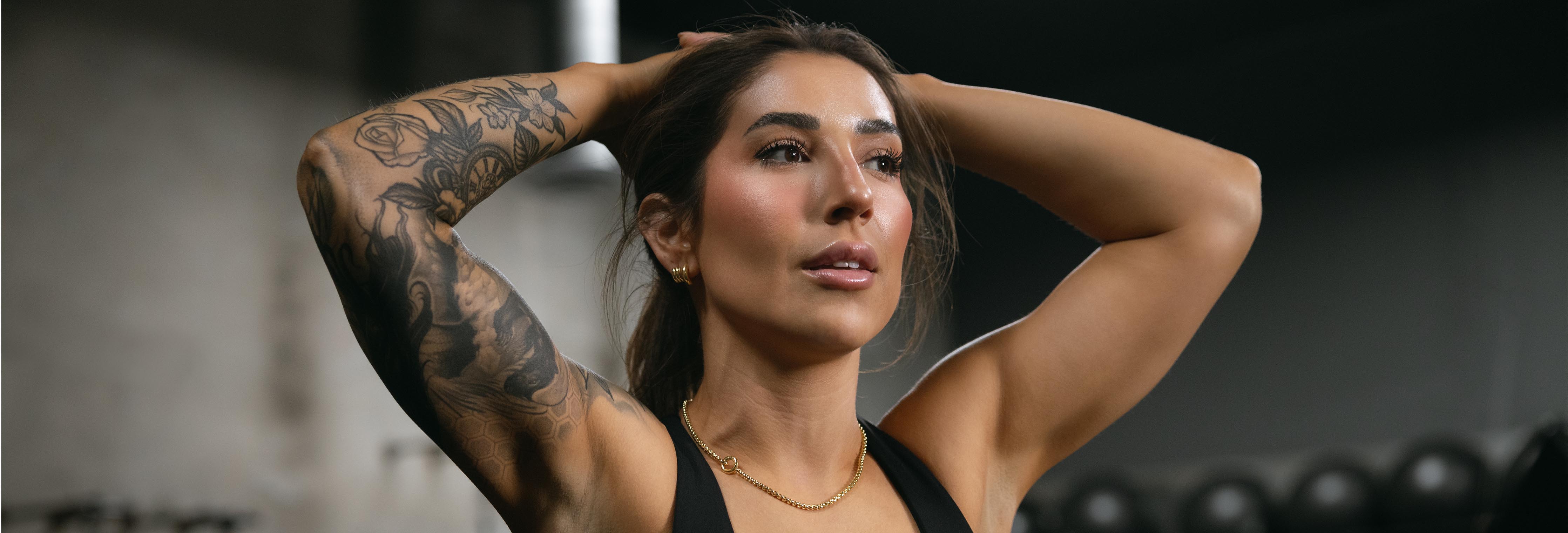 Athletic woman with tattooed arms stretching and pulling her hair back in a gym, pre workout pose