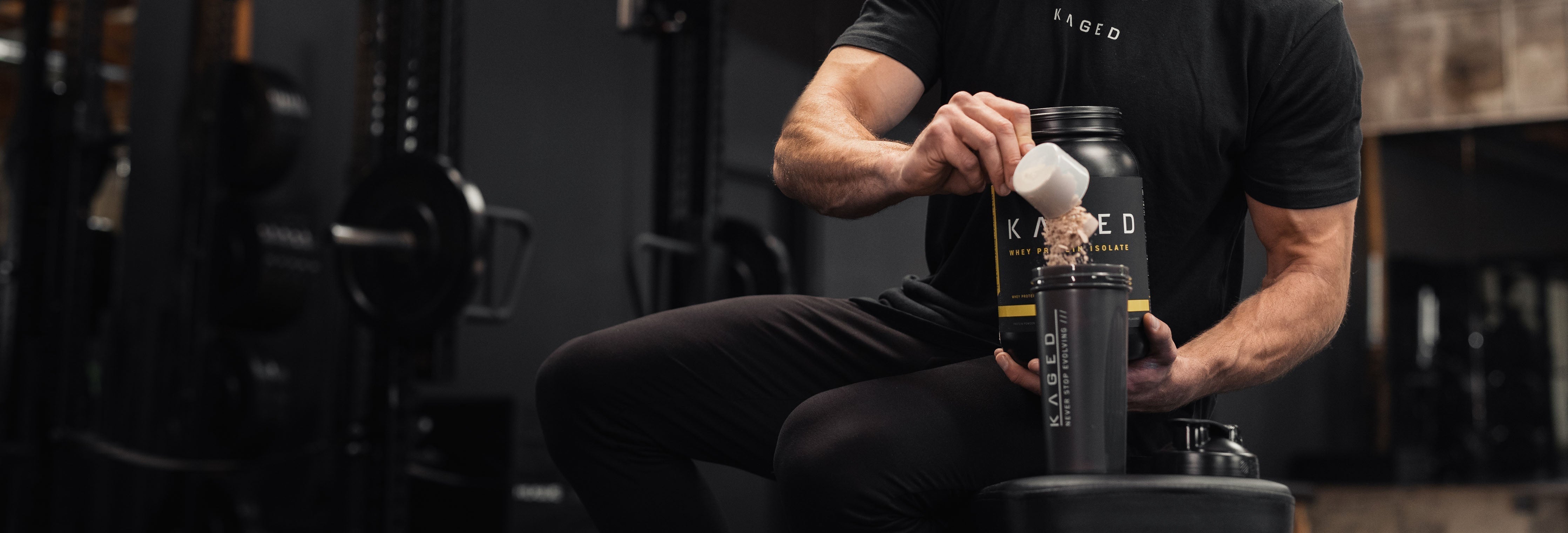 Athlete pouring KAGED protein powder into a shaker bottle while seated in a gym