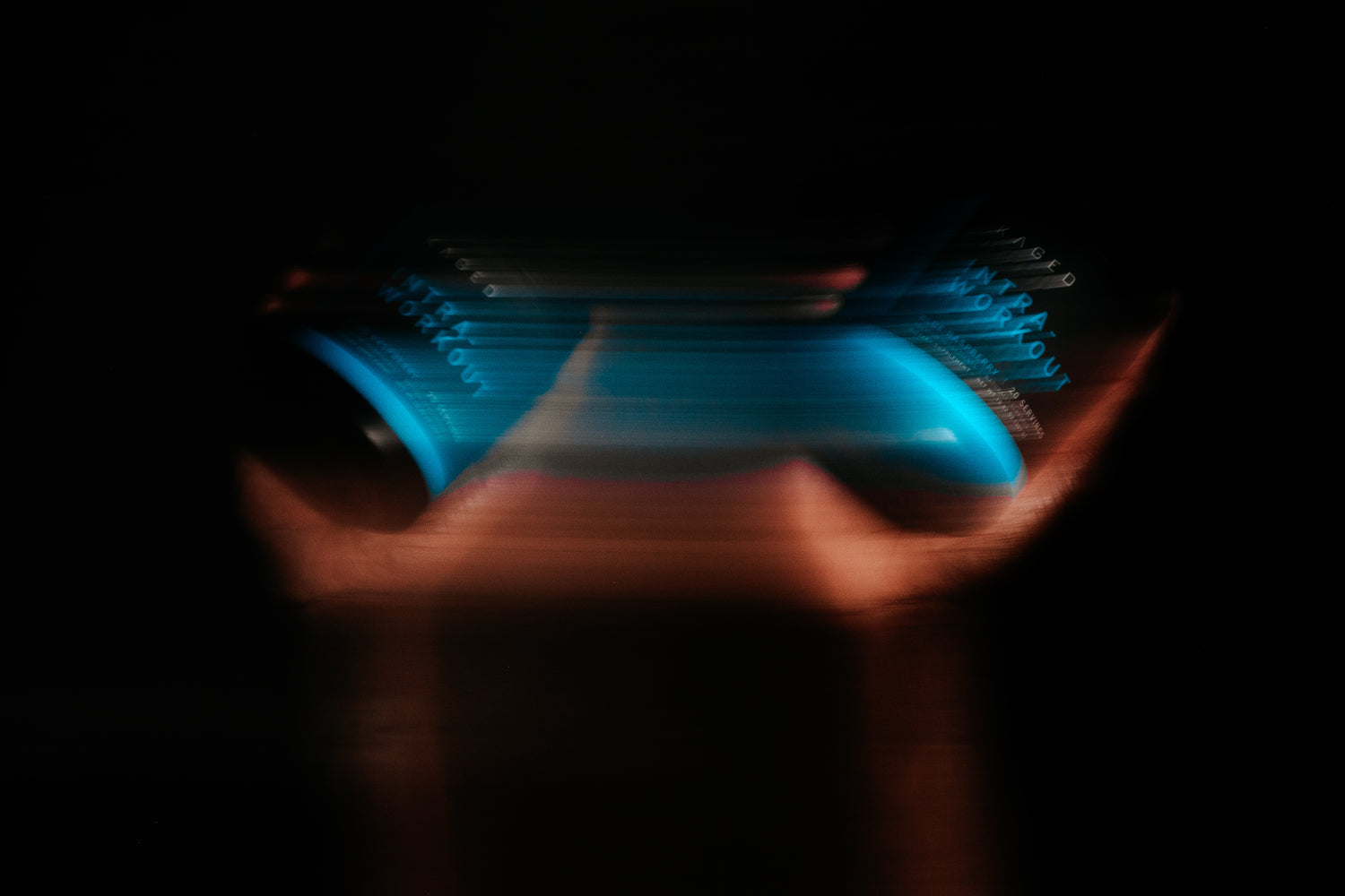 Blurred blue supplement tub held between hands with motion blur; faint 'workout' text visible