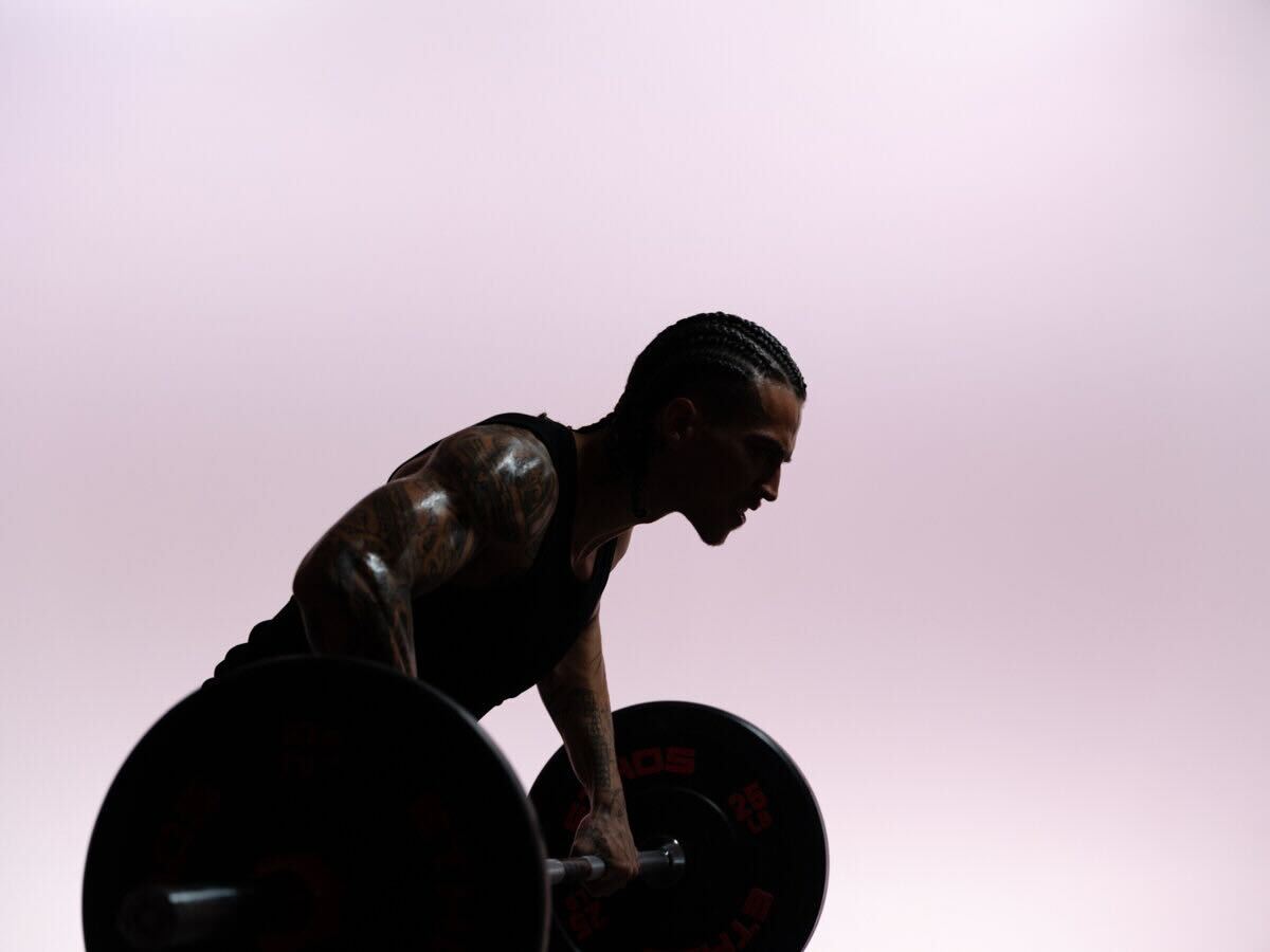 Athlete performing a bent-over barbell row in silhouette against a pale pink background