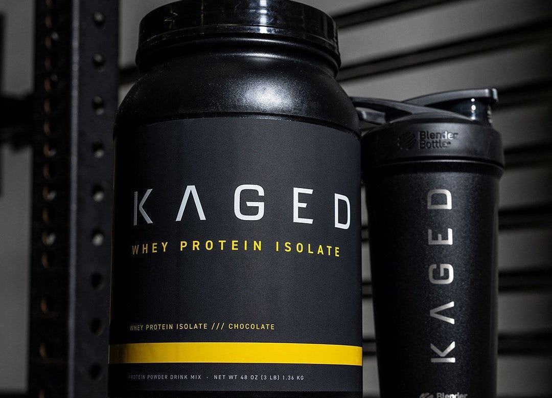 Kaged Whey Protein Isolate tub and Kaged Blender Bottle on gym bench.