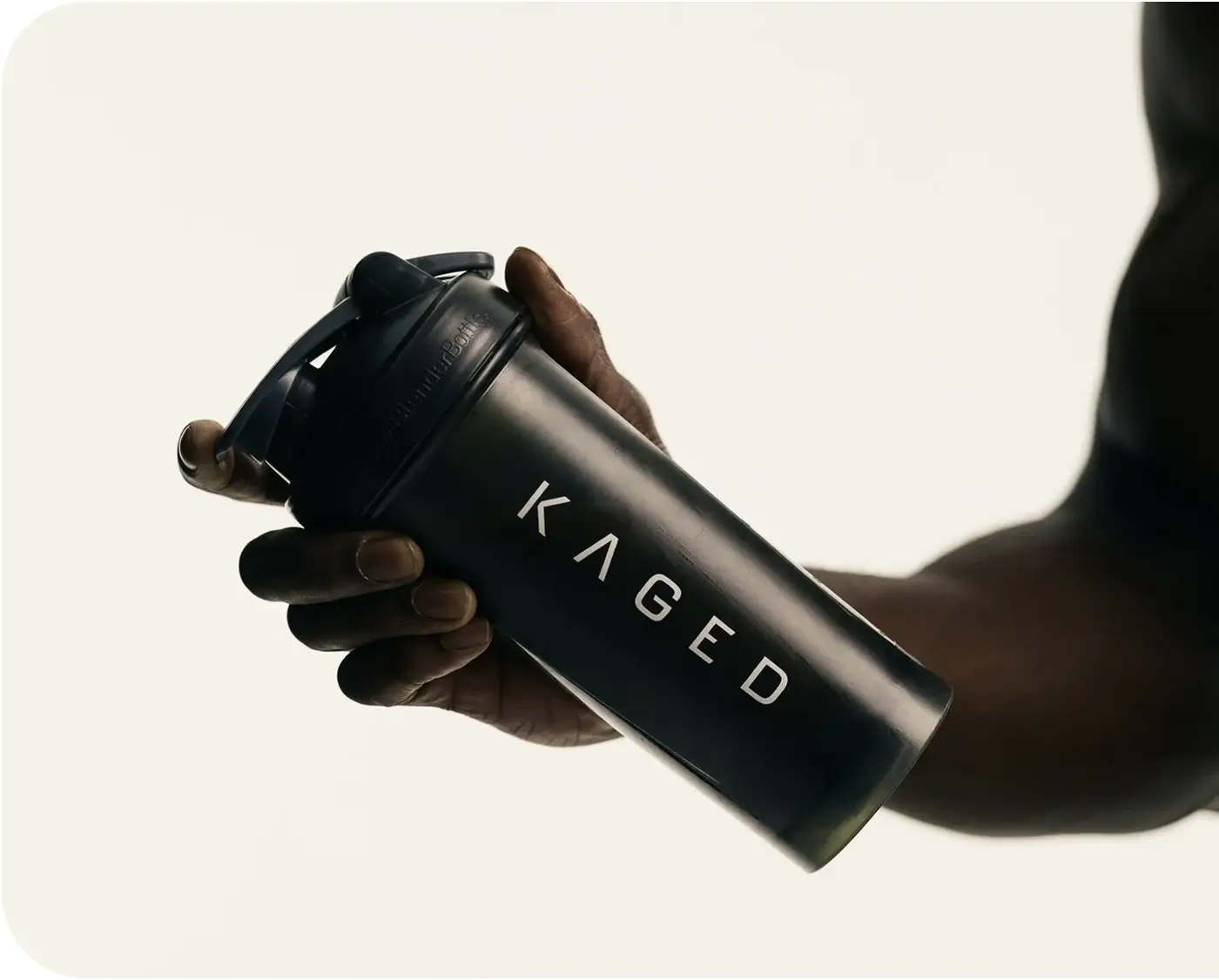Angled view of KAGED shaker bottle showcasing white KAGED logo and flip-top lid held in a hand against a light neutral background